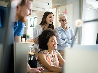 A group of professionals gathered around a computer, engaged in discussion and collaboration in a modern office setting.